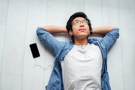 Happy asian man in shirt on the floor. with phone. listening musicの写真素材