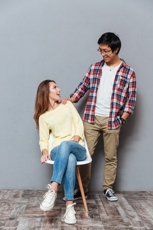 Full length portrait of a happy smiling couple looking at each other isolated on the gray backgroundの写真素材
