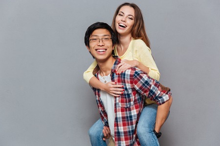 Portrait of a young multiracial couple enjoying piggyback ride isolated on the gray backgroundの写真素材
