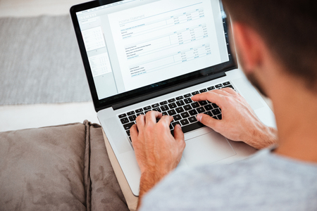 Cropped image of a young man typing on his laptop while sitting on sofa. Focus on hands typing.の写真素材
