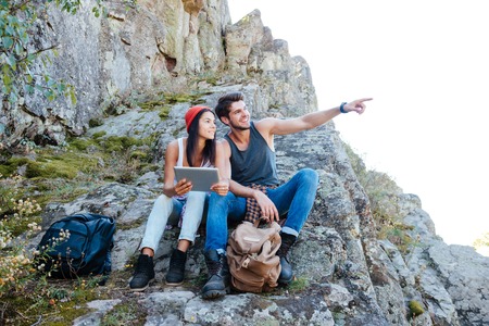 Happy smiling young couple resting with tablet computer while hiking at mountainsの写真素材