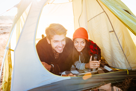 Portrait of a smiling couple lying in tent and using tablet computer outsideの写真素材