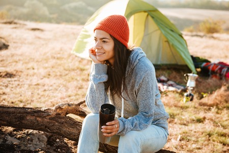 Young woman with tea sitting on log near the tentの写真素材