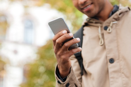 Cropped photo of young dark skinned man using his cellphone on the street.