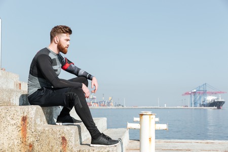 Young runner sitting on stairs near the sea. looking away.の写真素材