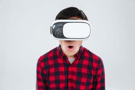 Image of surprised man dressed in casual shirt in a cage and wearing virtual reality device. Isolated over white background. Look at camera.の写真素材