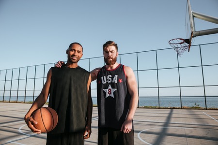 Two young basketball players standing together at the playground and looking at cameraの写真素材