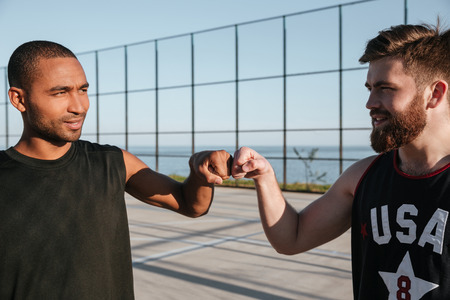 Portrait of a two smiling basketball players fist bumping while standing at the playgroundの写真素材