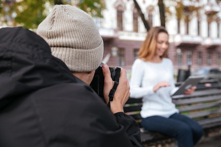 Back view of man photographer taking pictures of happy lovely young woman in parkの写真素材