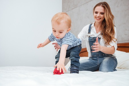 Happy young mother playing with her little son on bed at home