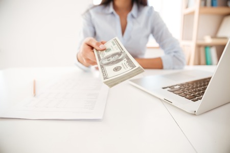 Cropped image of businesswoman dressed in white shirt sitting in her office and give money to cameraの写真素材