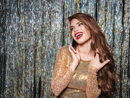 Happy cute young woman in evening dress talking on cell phone over shining background