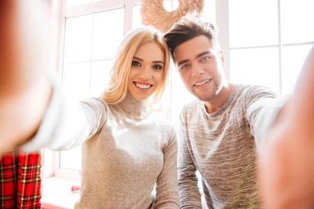 Couple in sweaters makes selfie in house.の写真素材