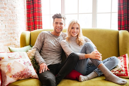 Young couple in sweaters on sofa in house. looks at cameraの写真素材