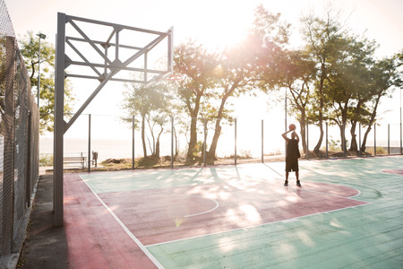 Photo of young african basketball player in the street with ball. Looking at basketball hoop.の写真素材