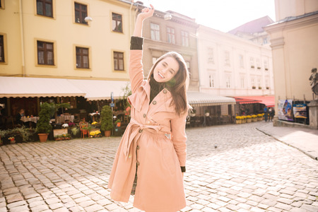 Cheerful joyful young woman standing with raised hand in old cityの写真素材