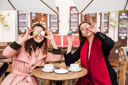 Two funny young women sitting and having fun together in outdoor cafeの写真素材