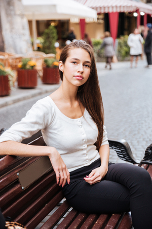 Beautiful young woman sitting on the bench in old townの写真素材