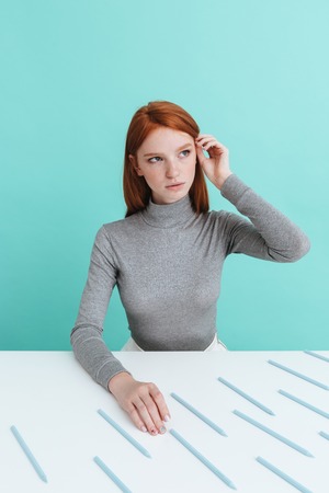 Cute redhead young woman sitting at the table with pencils over blue backgroundの写真素材