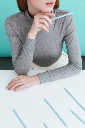 Closeup of attractive young woman sitting and holding pencil over blue background