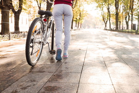 Cropped picture of young caucasian woman walking with her bicycle in the street