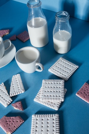 Top view of bottles with milk, cups and broken cookies over blue backgroundの写真素材
