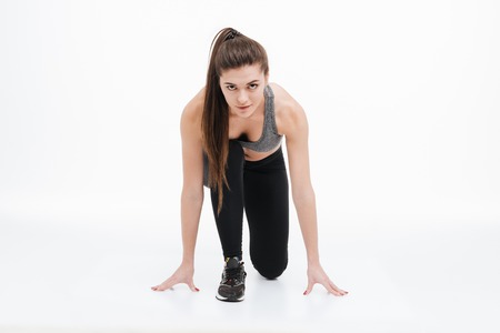 Portrait of a young sports woman standing in start position for running isolated on a white...