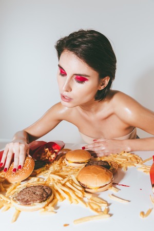 Attractive young woman with bright makeup eating fast food over white backgroundの写真素材