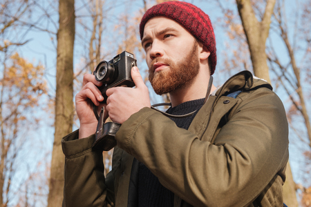 Image of serious bearded man using camera standing in the forest.の写真素材