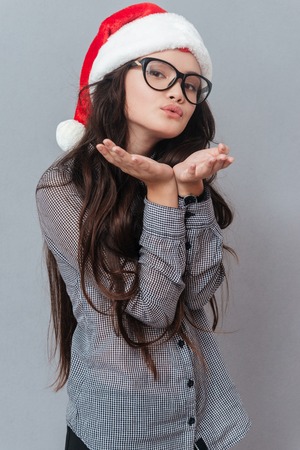 Vertical image of asian woman in christmas hat sands air kiss. Isolated gray backgroundの写真素材