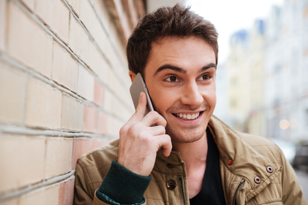 Portrait of happy young man walking on the street and looking aside while talking by his phone.の写真素材