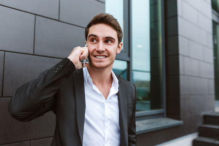 Business man in suit talking on phone and standing near the officeの写真素材