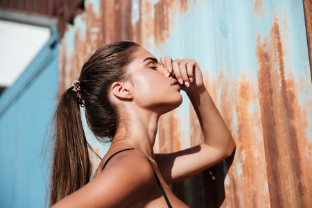 Sensual young woman with ponytail standing and touching her nose over rusty metal backgroundの写真素材