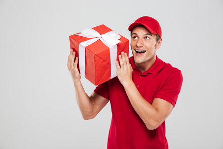Happy delivery man with christmas gift. looking away. isolated gray backgroundの写真素材