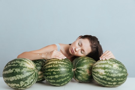Relaxed young woman lying and sleeping on green fresh watermelonsの写真素材