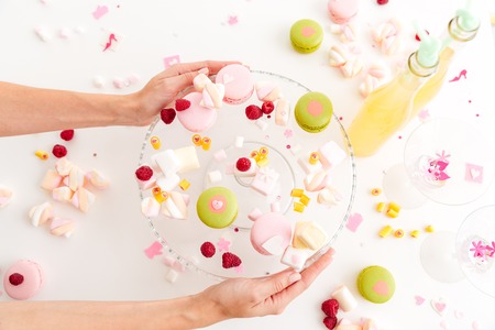Hands putting plate with macaroons and marshmallows on the table over white backgroundの写真素材
