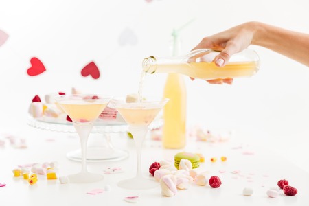 Hand pouring lemonade into glasses on the table with sweets over white background
