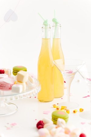 Two bottles of lemonade, glasses and macaroons on the table over white backgroundの写真素材