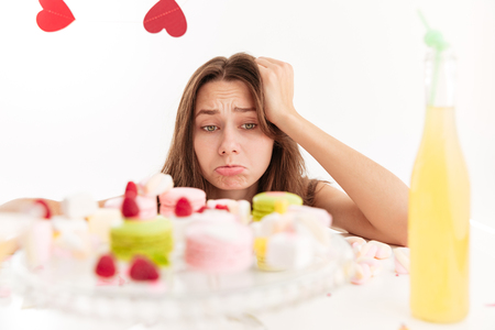 Sad upset young woman looking at sweests on the tableの写真素材