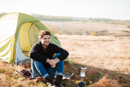 Young happy man sitting outdoors with tent on the backgroundの写真素材