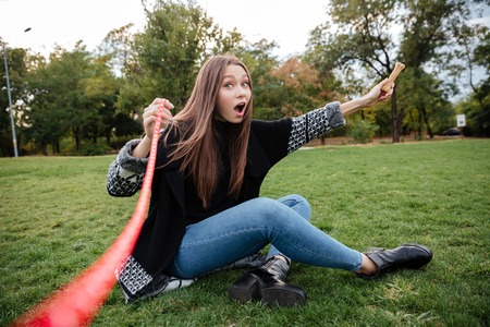 Playful lovely young woman sitting on lawn and playing with dog in parkの写真素材