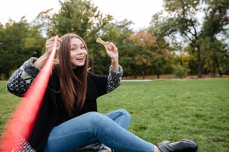 Smiling relaxed young woman sitting and throwing bone to her dog in parkの写真素材