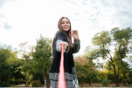Happy beautiful young woman playing with dog on leash in park