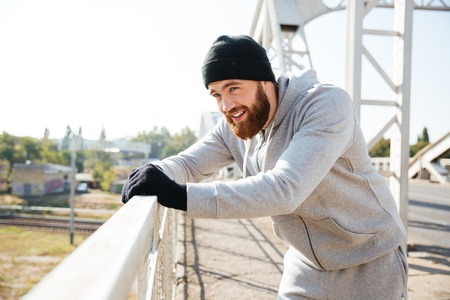 Tired handsome young man athlete standing and resting at the urban bridgeの写真素材