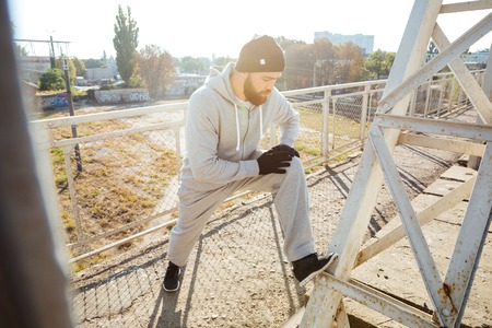 Portrait of a handsome bearded sportsman stretching legs outdoorsの写真素材