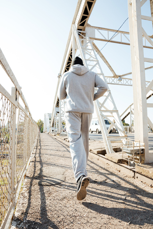 Back view of a jogger in sportswear running along the bridgeの写真素材