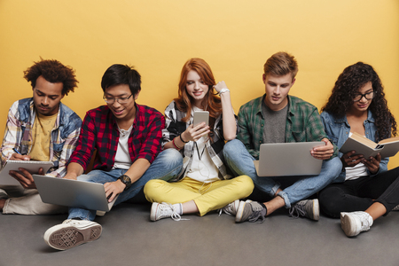 Multiethnic group of concetrated young friends with laptops studying together over yellow backgroundの写真素材