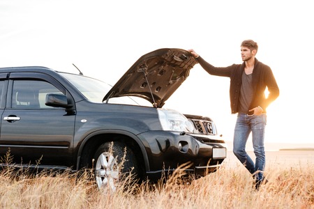 Concentrated young man holding hands on vehicle hood and looking inside it while standing outdoorsの写真素材