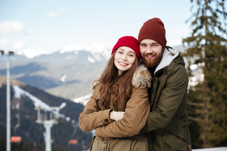 Photo of young attractive loving couple standing over mountains looking at camera and hugging.の写真素材