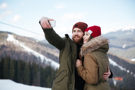 Picture of young attractive loving couple take a selfie over mountains. Looking at phone.の写真素材